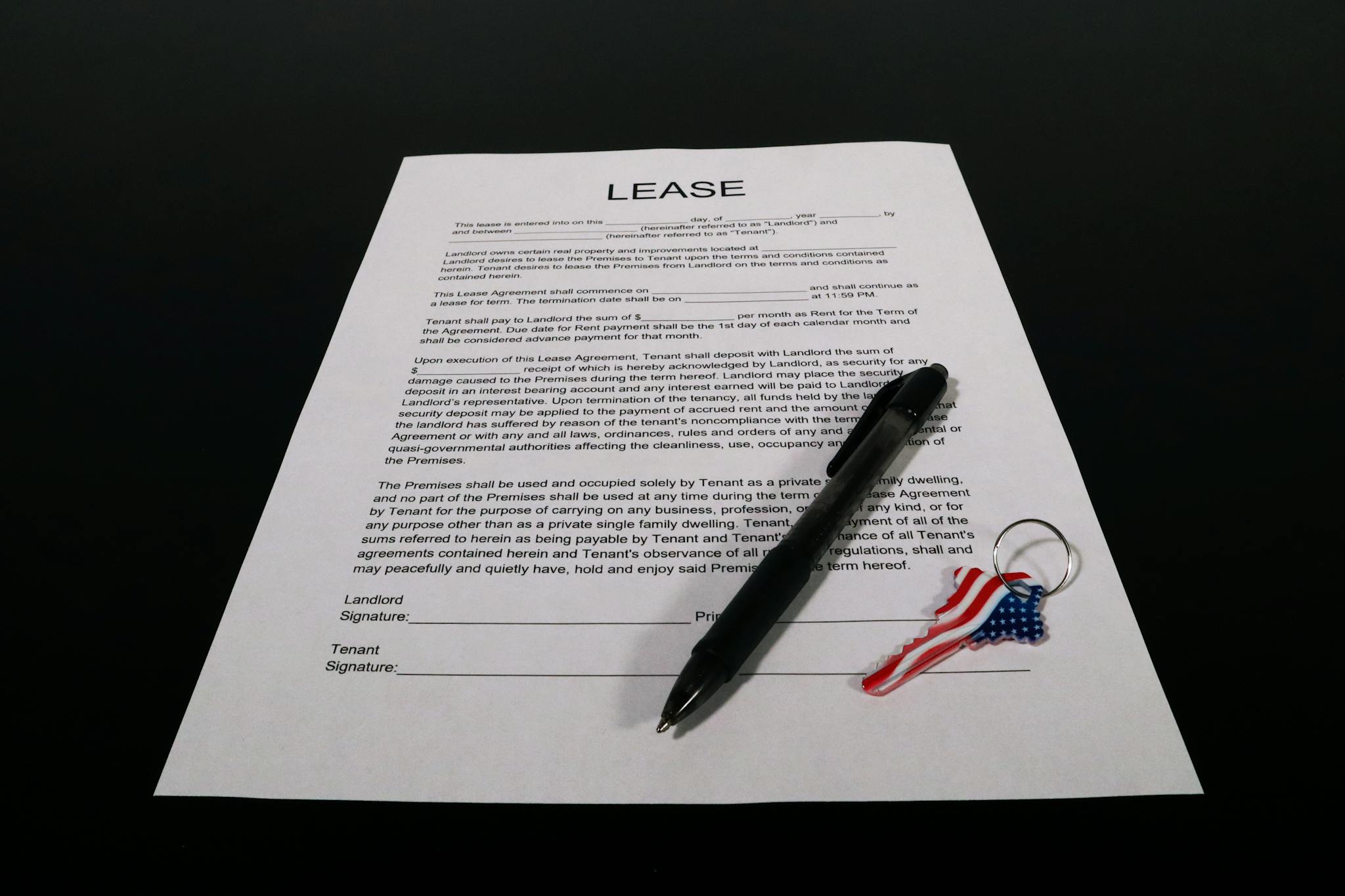 Lease agreement document with pen and American flag keychain on a black table.