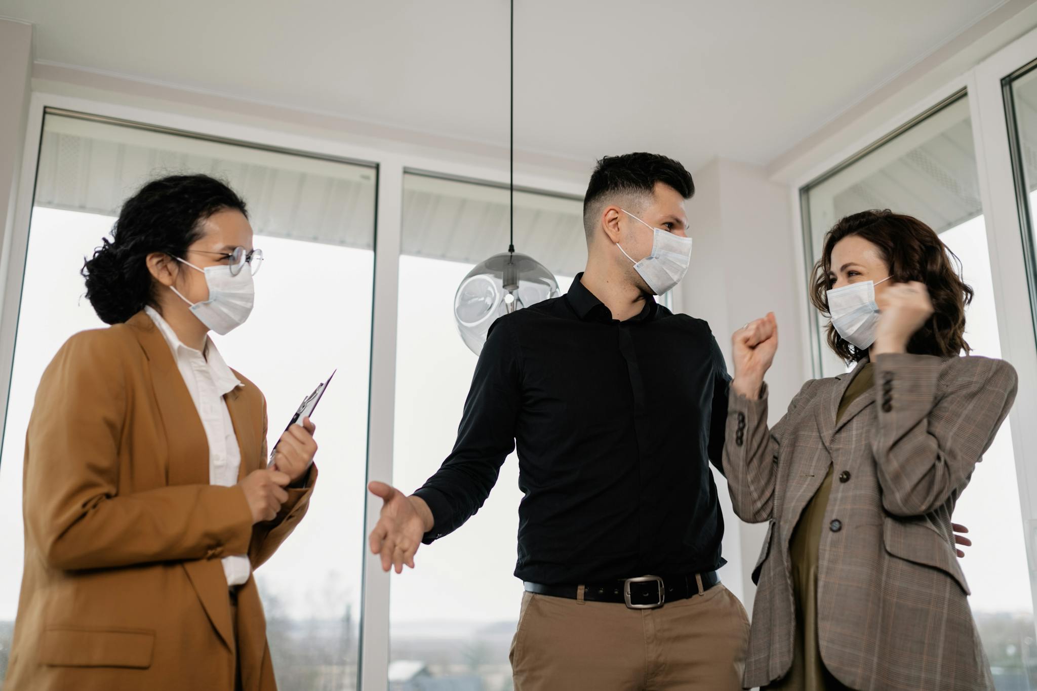 Three adults with face masks discussing real estate indoors joyfully.